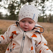 Beige bambumössa med klövermönster från Geggamoja på en baby i beige fleecejacka utomhus.