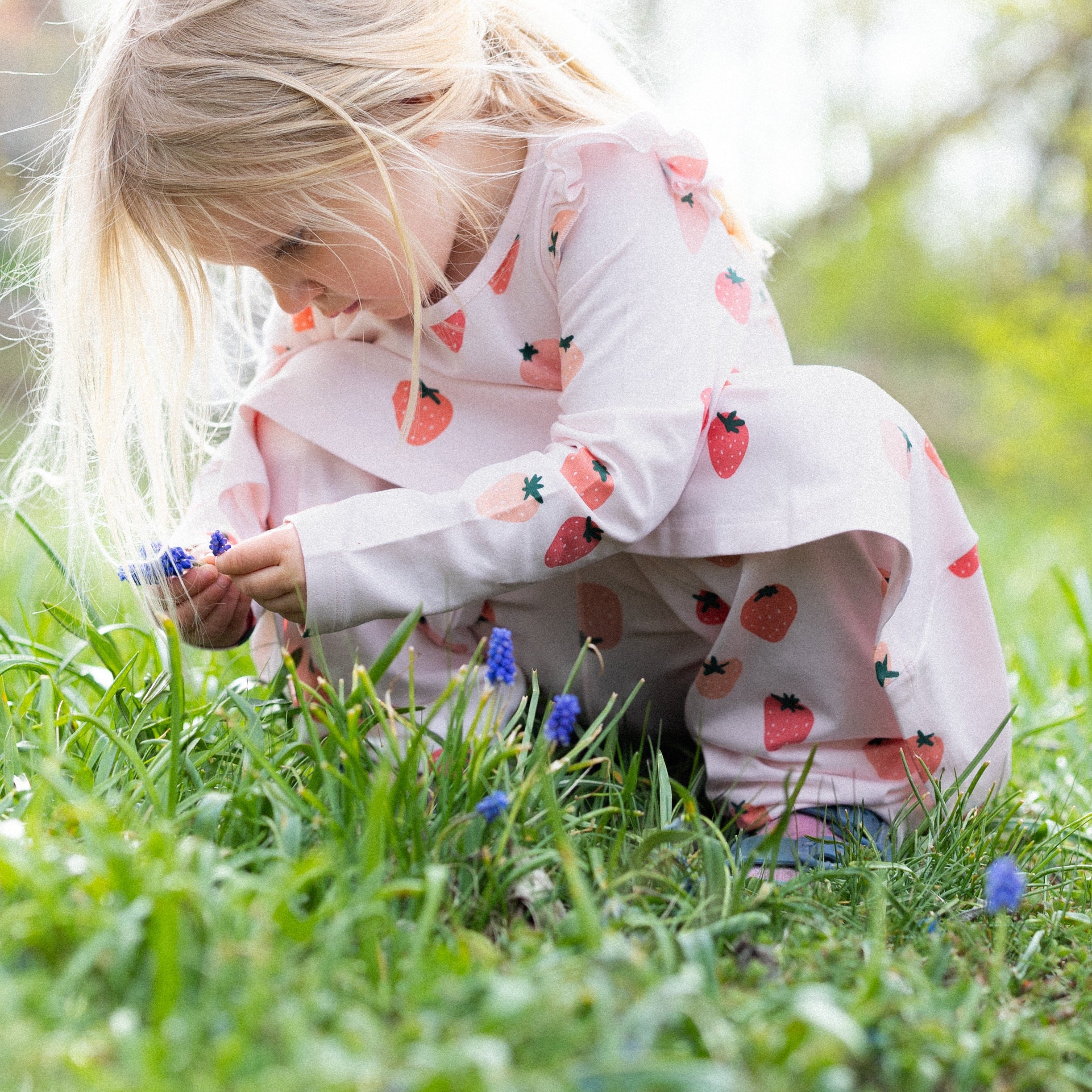 Rosa Geggamoja leggings med jordgubbsmönster i mjuk bambu på barn som plockar blommor i gräset.