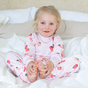 Rosa tvådelad pyjamas i mjuk bambu med mönster av jordgubbar på barn i en säng från Geggamoja.