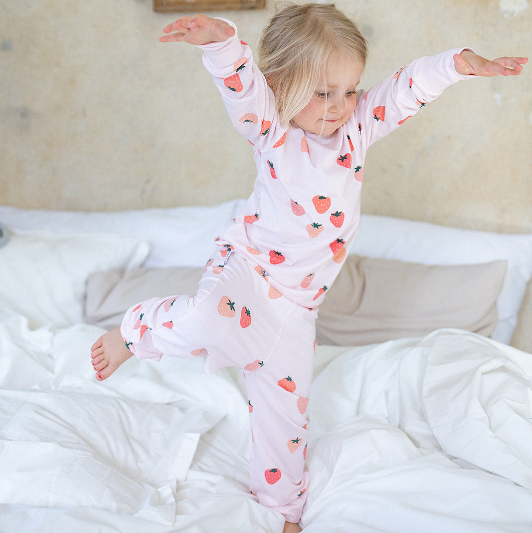 Rosa tvådelad pyjamas i mjuk bambu med jordgubbsmönster från Geggamoja på ett barn i en säng.
