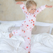 Rosa tvådelad pyjamas i mjuk bambu med jordgubbsmönster från Geggamoja på ett barn i en säng.