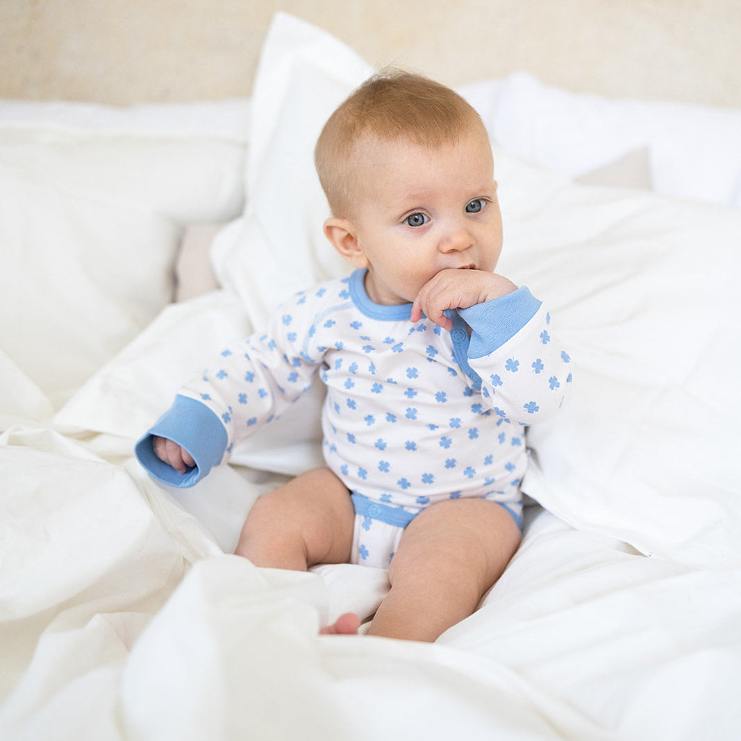 Blåmönstrad Geggamoja-body i bambu med klövermönster på en baby i en vit säng.