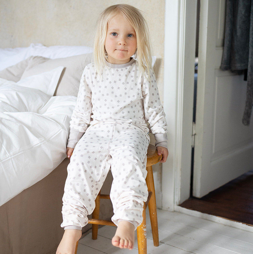 Beige klövermönstrad pyjamas i mjuk bambu från Geggamoja på ett barn i sovrumsmiljö.