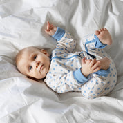 Geggamoja bambupyjamas med blått klövermönster och tvåvägsdragkedja på bebis i en mjuk säng.