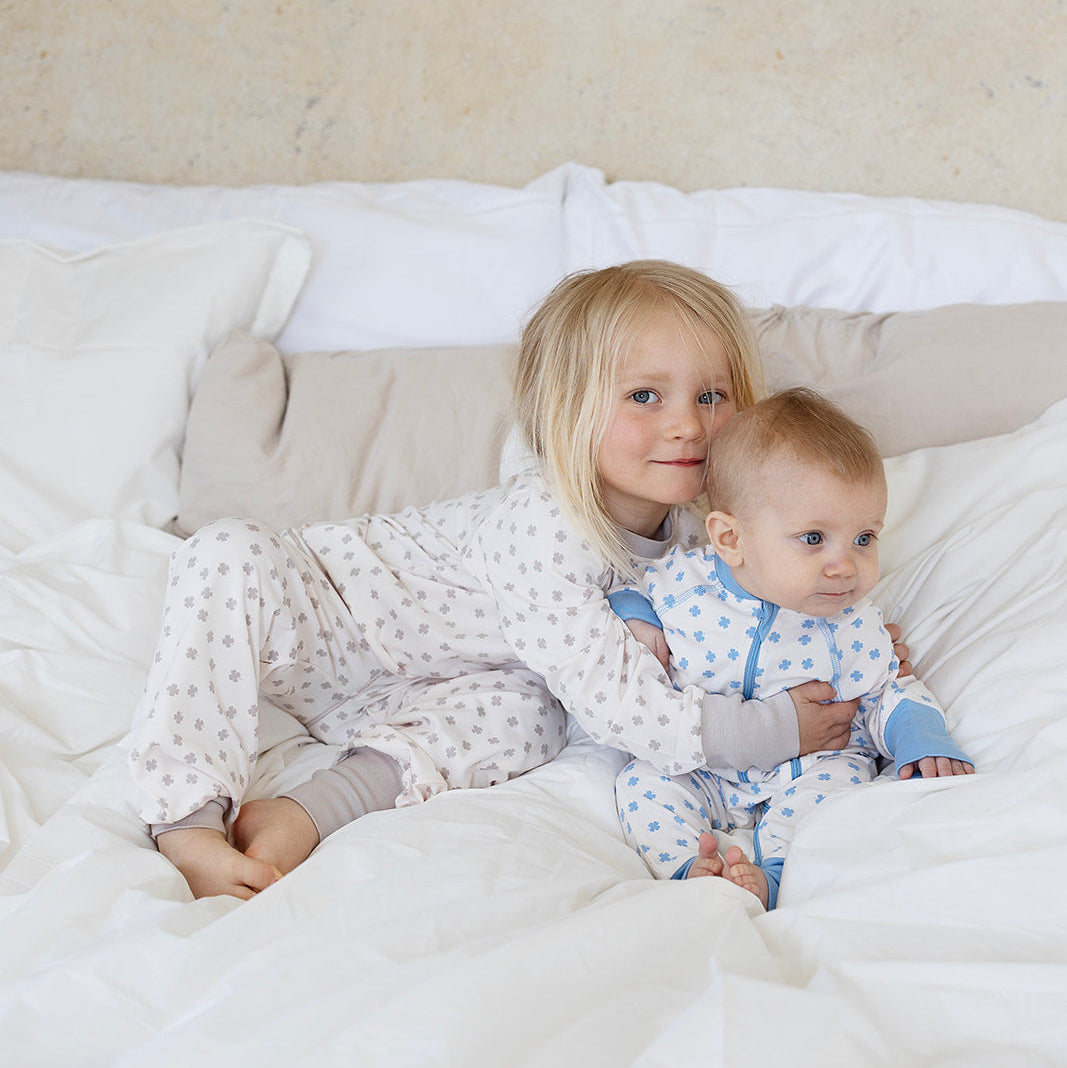 Beige tvådelad bambupyjamas med klövermönster på barn i en mjuk säng från Geggamoja.