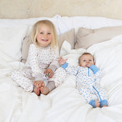 Blå klövermönstrad bambupyjamas från Geggamoja på en baby i säng med ett barn i matchande pyjamas.